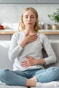 Concept of mental health. Woman sitting on couch and doing calming breathing exercises after panic attack. Female inhaling and exhaling to deep breath. Self-control, anxiety relief concept