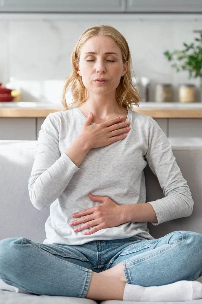Concept of mental health. Woman sitting on couch and doing calming breathing exercises after panic attack. Female inhaling and exhaling to deep breath. Self-control, anxiety relief concept