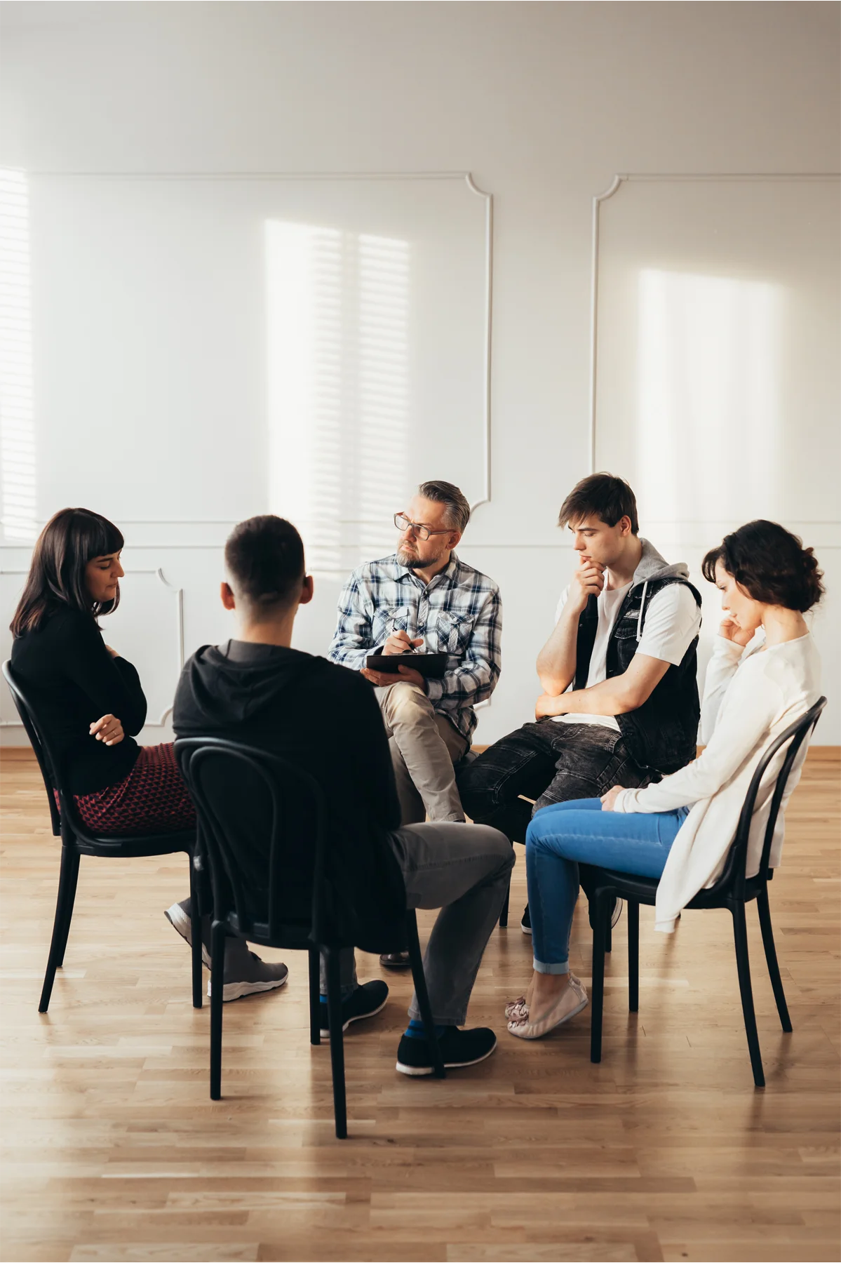Group of people of different ages sits in a circle during a meeting with a professional therapist